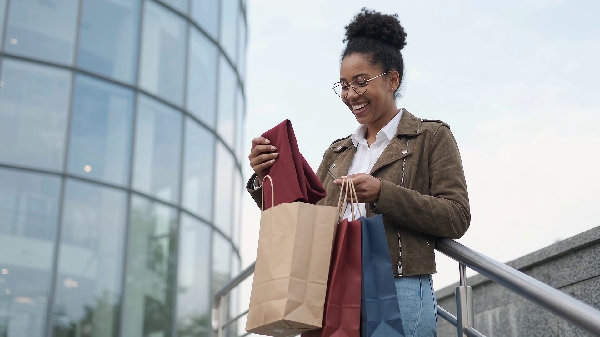 A young woman smiles as she takes a burgundy dress out of her shopping bags